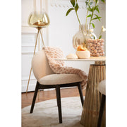 Eetkamerscène: ronde tafel met stoel, gouden accenten, glazen vaas met bloemen en een staande lamp.