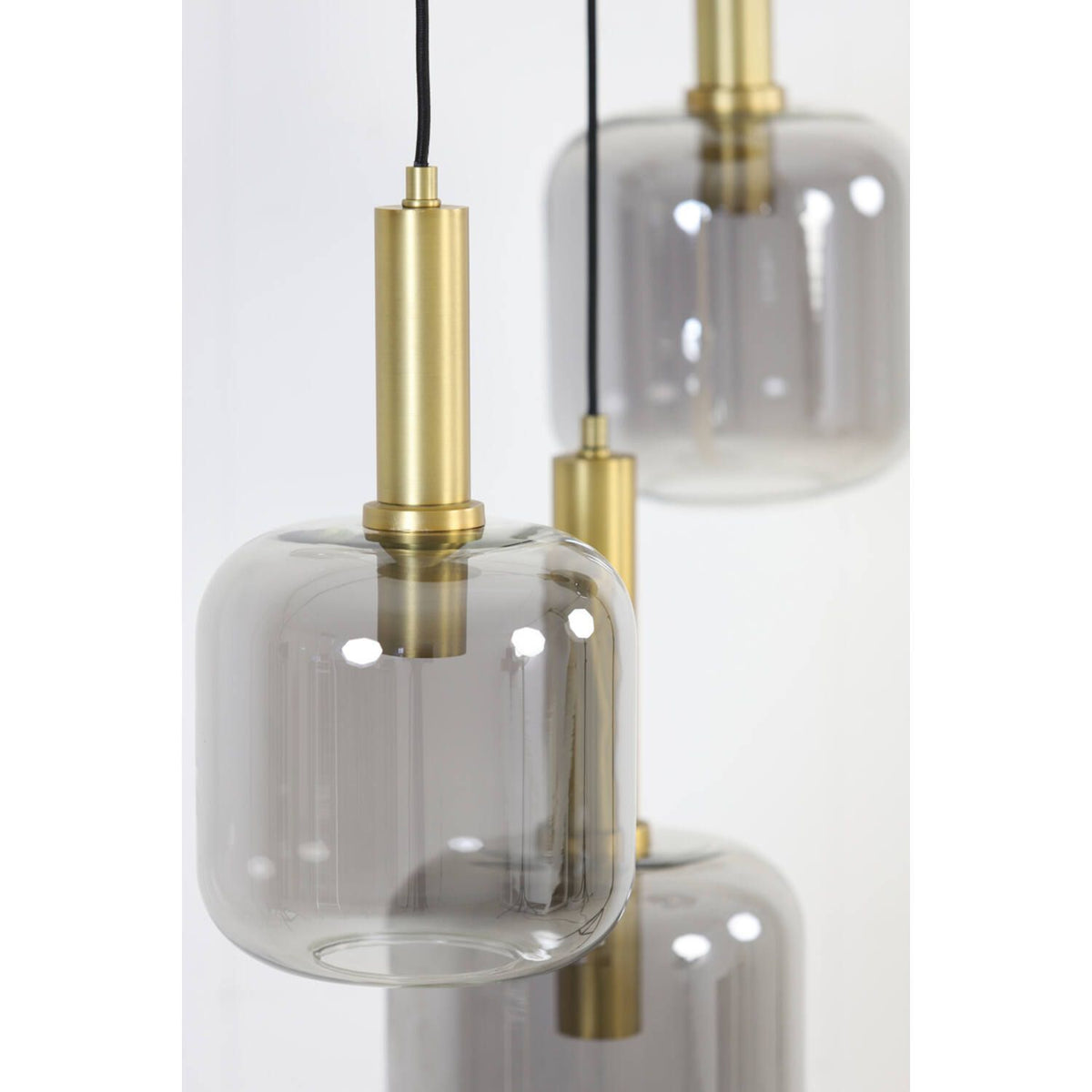 Drie hanglampen met rookkleurige glazen kappen en messingkleurige details hangen tegen een witte achtergrond.