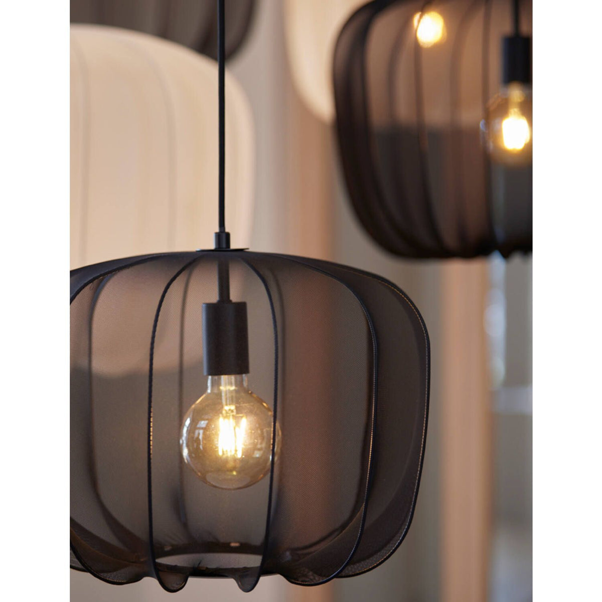 Twee zwarte hanglampen van gaas met zichtbare lampen, hangend binnenshuis.