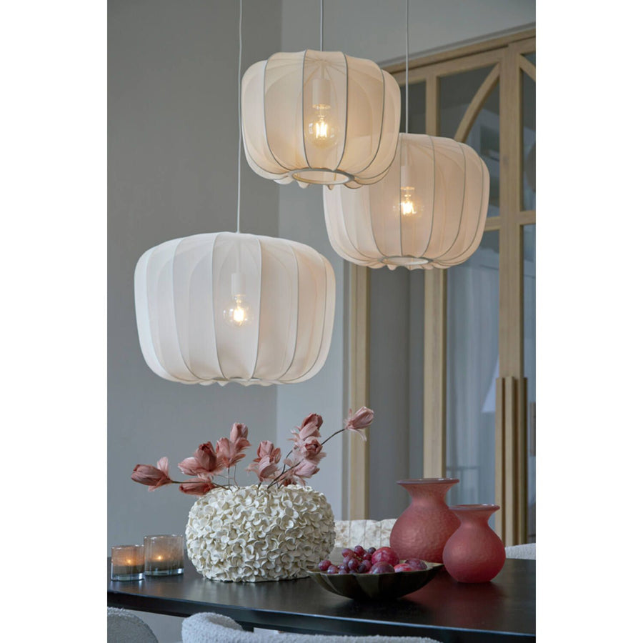Boven een tafel met bloemen en vazen ​​hangen drie witte stoffen hanglampen.