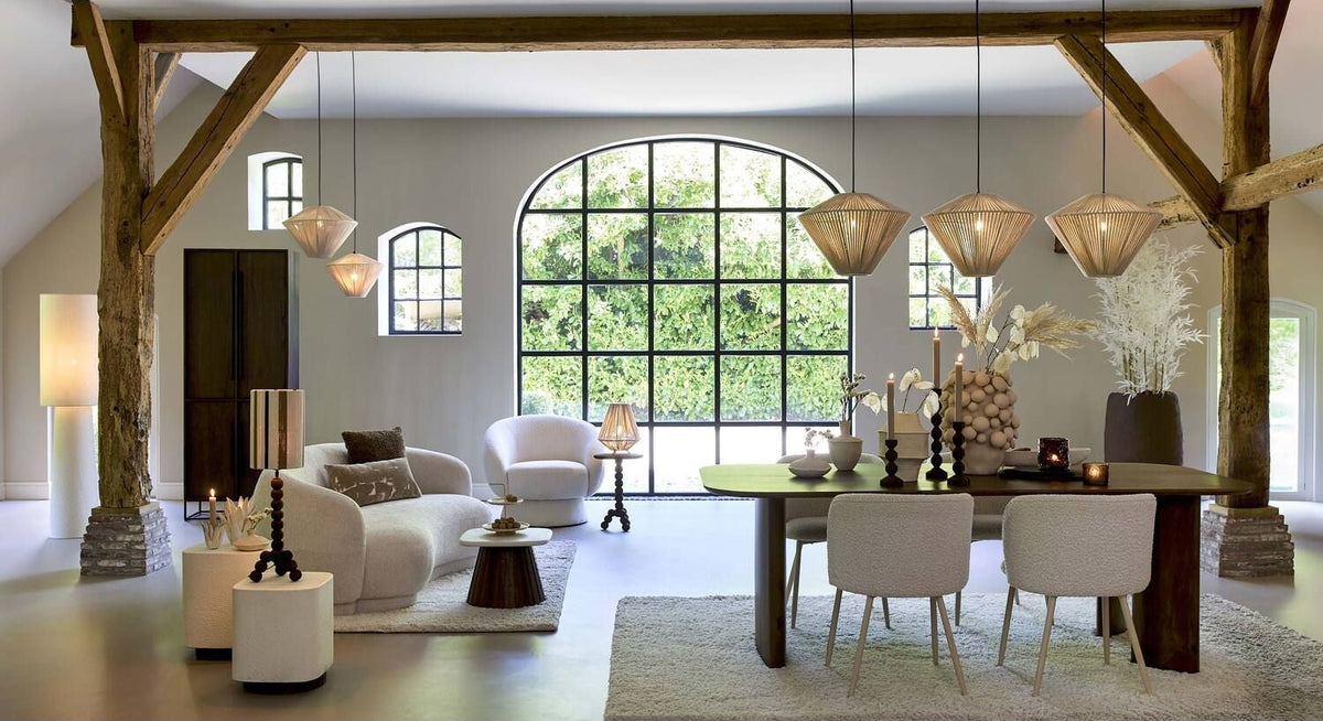 Woon- en eetkamer met houten balken, een groot raam en moderne meubels in neutrale tinten.