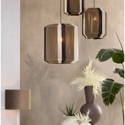 Drie hanglampen boven een eettafel. Bruine, beige en witte gestreepte kappen, met links een wandlamp en een vaas met planten.