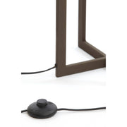 Detailopname van de voet van een staande lamp en een zwarte voetschakelaar op een witte achtergrond.