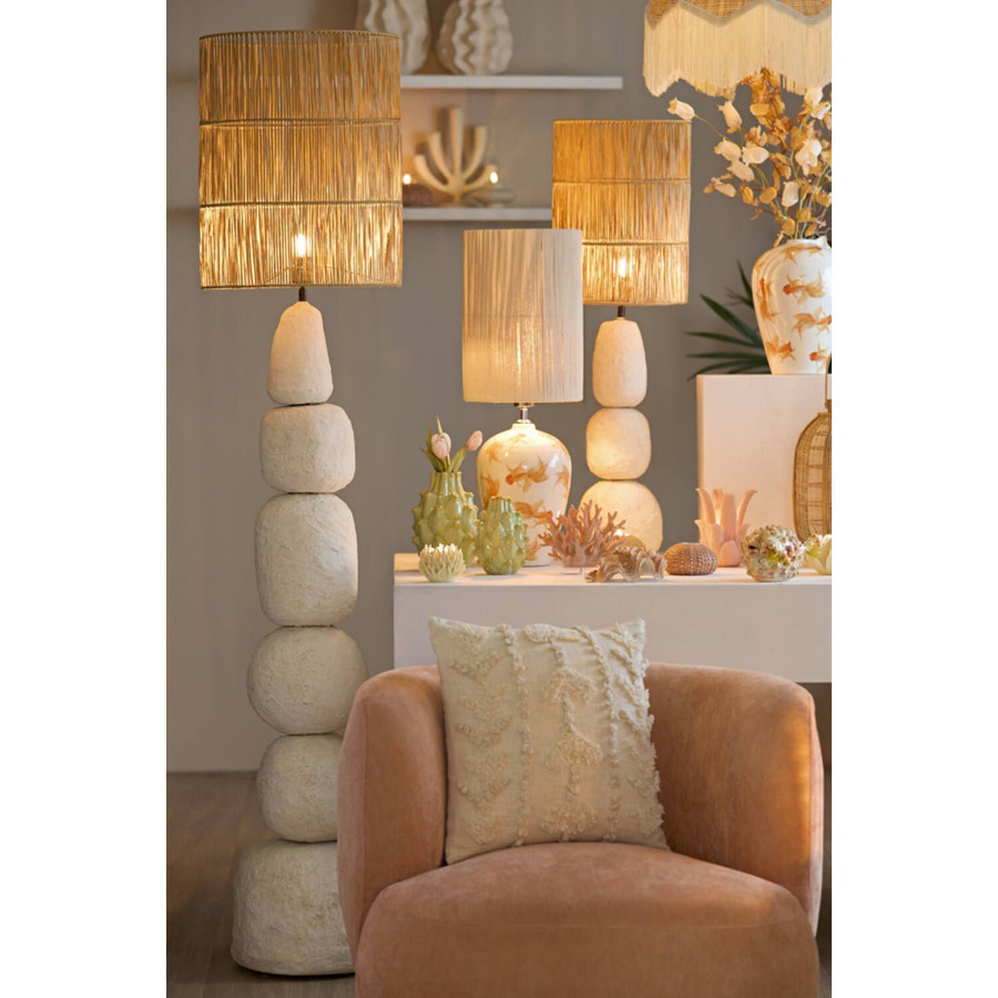 Een woonkamer met lampen van gestapelde stenen, een perzikkleurige stoel en decoratieve objecten op een witte tafel.
