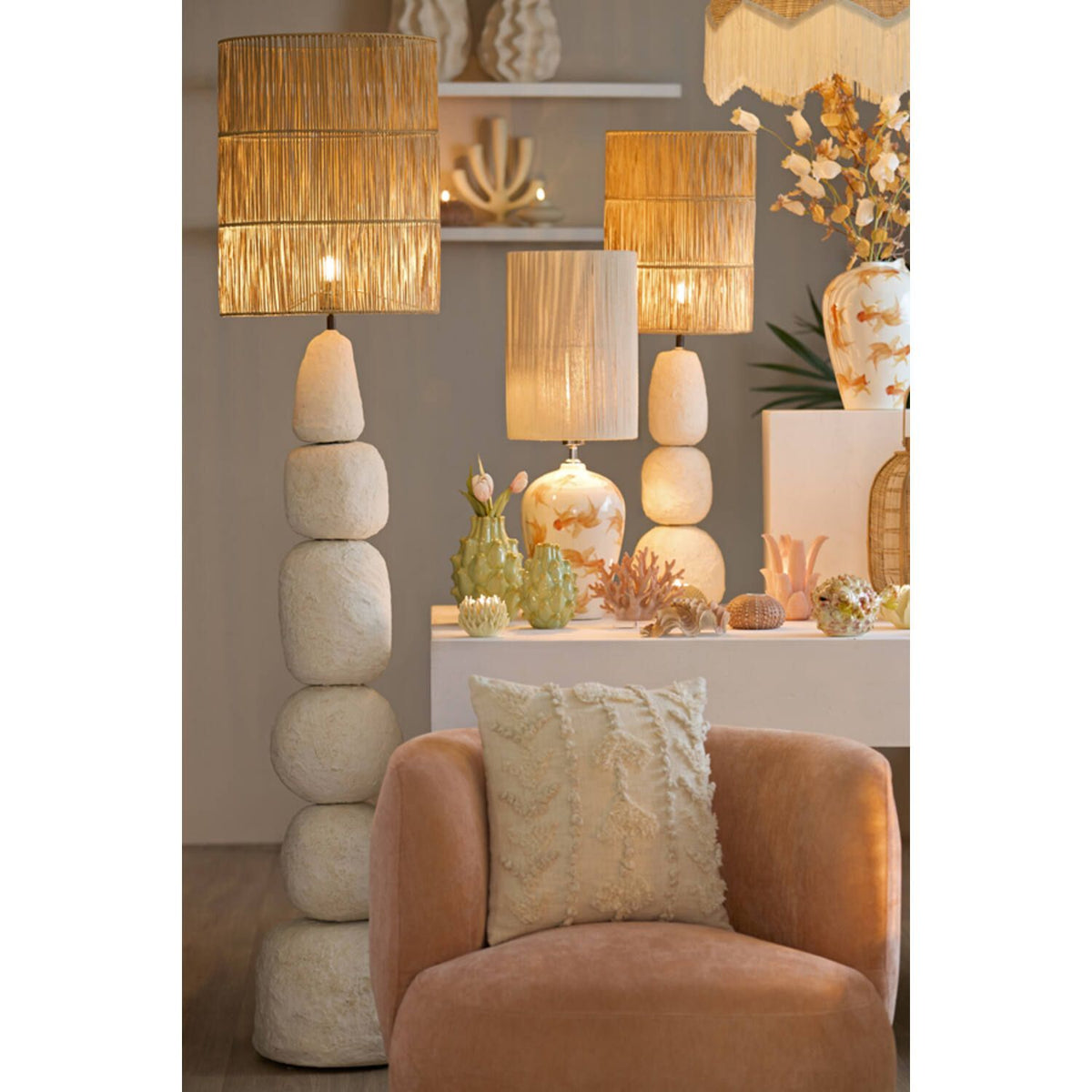 Een woonkamer met lampen van gestapelde stenen, een perzikkleurige stoel en decoratieve objecten op een witte tafel.
