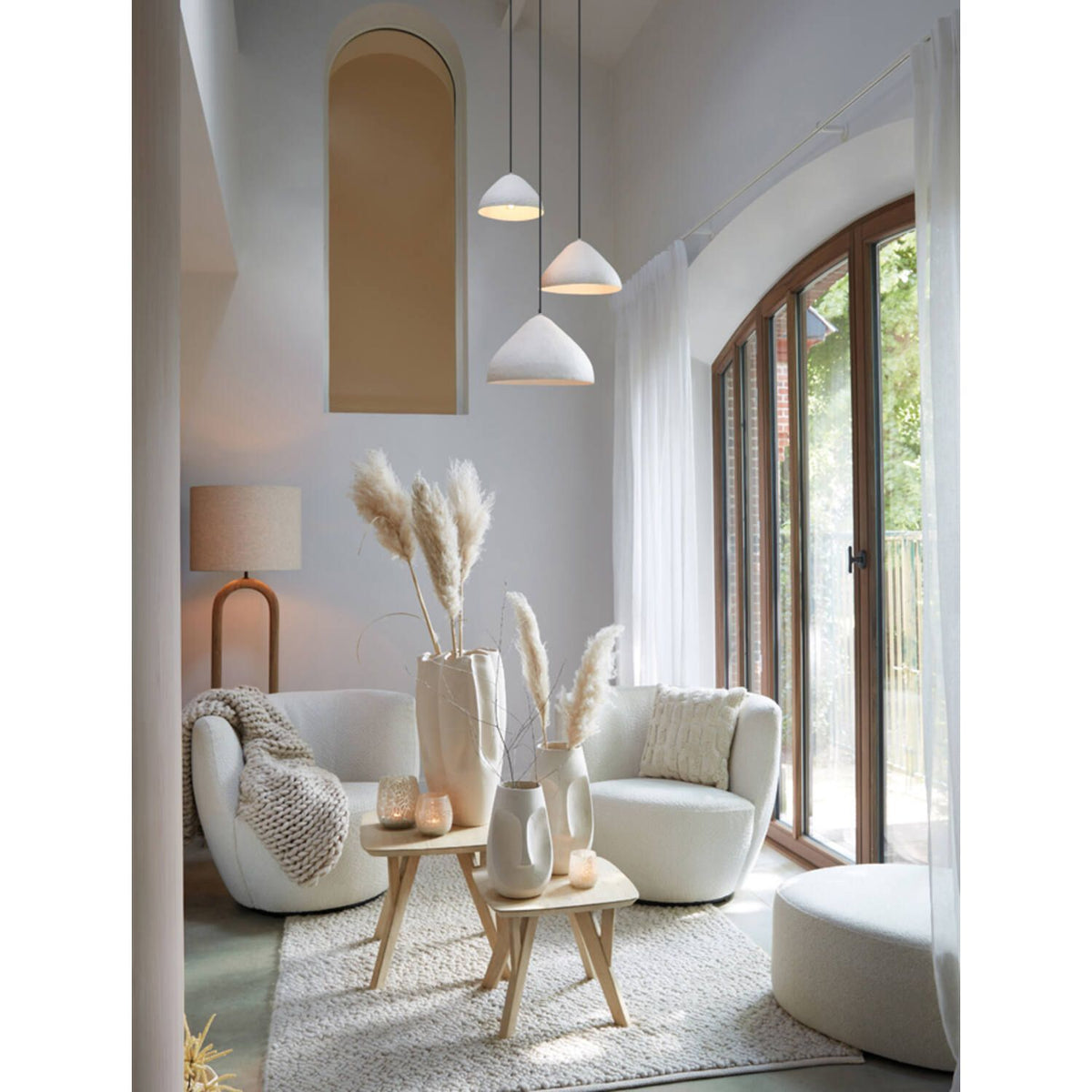 Gezellige woonkamer met crèmekleurig meubilair, decoratie van pampasgras, natuurlijk licht en hanglampen.