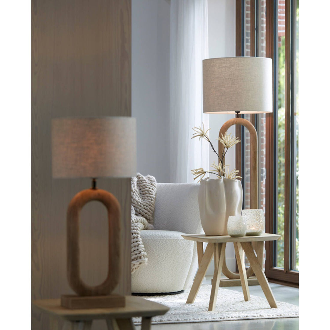 Tafellamp en staande lamp met neutrale kappen in een woonkamer. Bijzettafel met vaas en kaars.