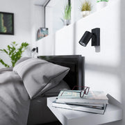 Zwarte wandlamp met cilindrische verstelbare GU10 spot, rechthoekige wandplaat en geïntegreerde schakelaar.